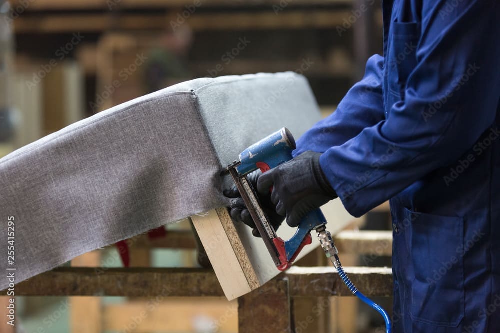 Primer plano de un joven en una fábrica de muebles que monta una parte del sofá con una grapadora